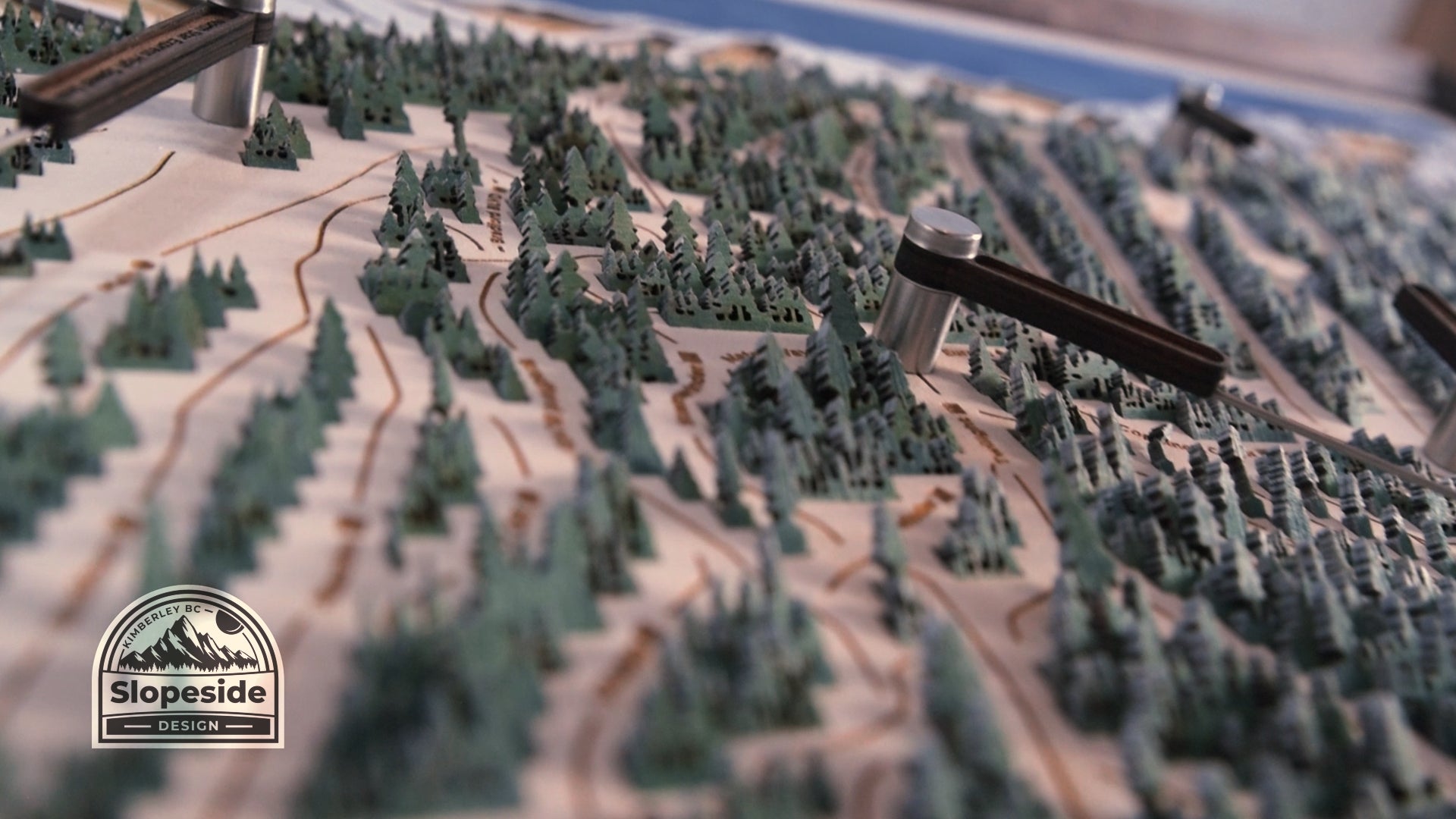 Load video: Close-up video showcasing the intricate details of a handcrafted wooden topographic map. The camera moves slowly over the layered contours, highlighting precise laser-cut edges, delicate tree silhouettes, and the natural wood grain. Light shifts across the surface, emphasizing the depth and texture of the piece.